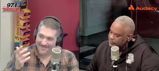 A middle-aged white man with gray hair and a plaid shirt blathers into a microphone while his co-host, a Black man in a black hoodie, listens.